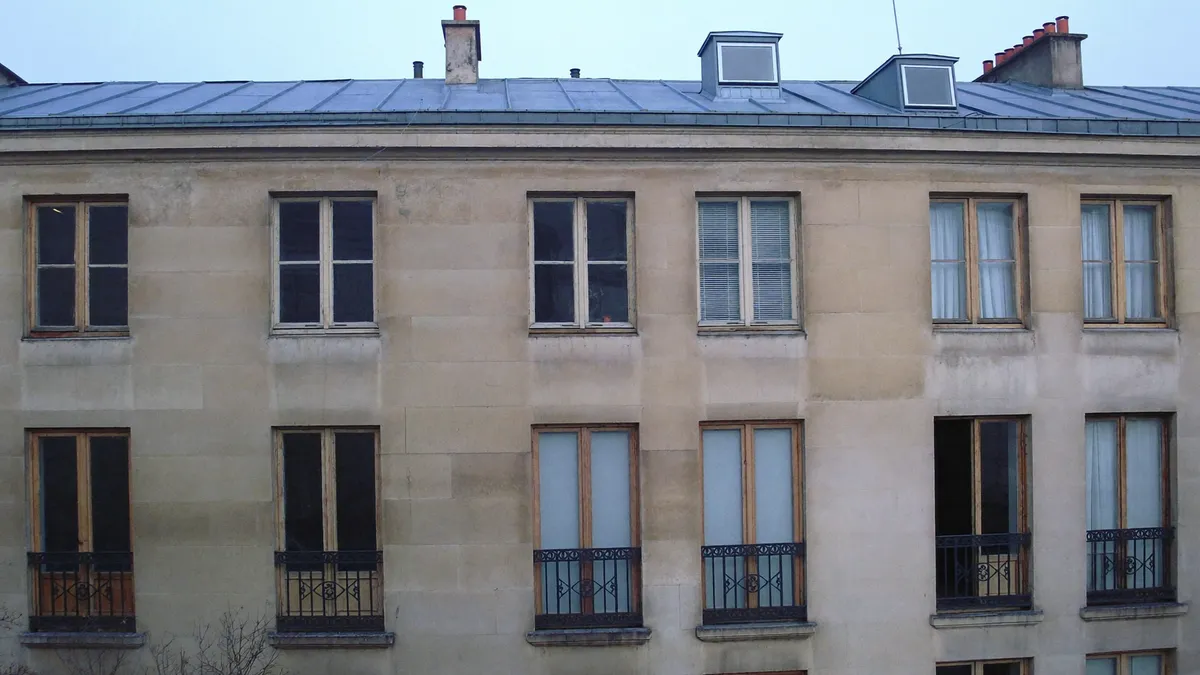 Façade parisienne ancienne aux fenêtres simple vitrage sous un ciel gris, toiture en zinc
